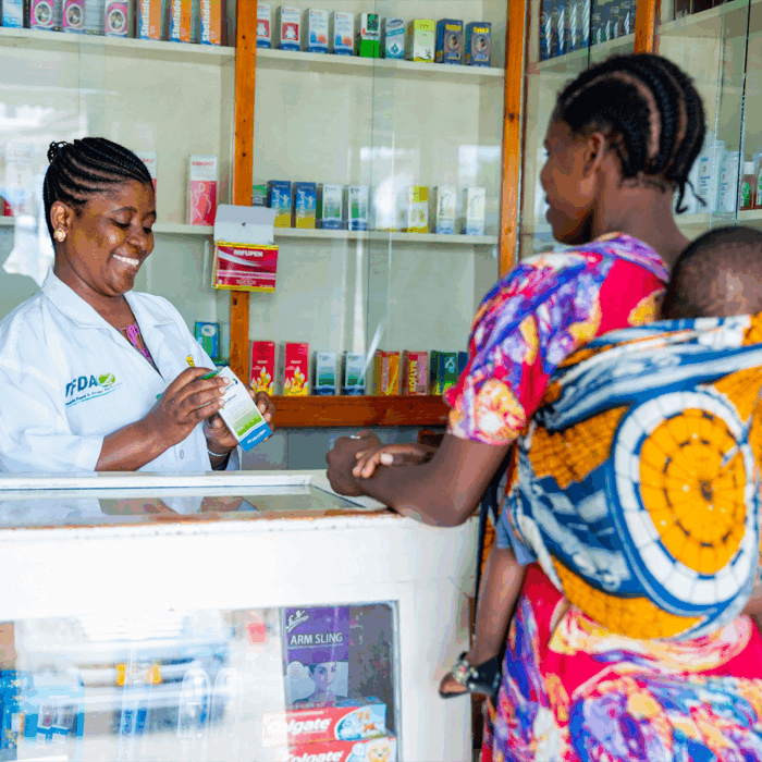 Building Integrated Systems for Financing Essential Medicines and Other Health Products — From Silos to Systems (Pharmacist in Tanzania dispenses medicine to a moth carrying her young child)