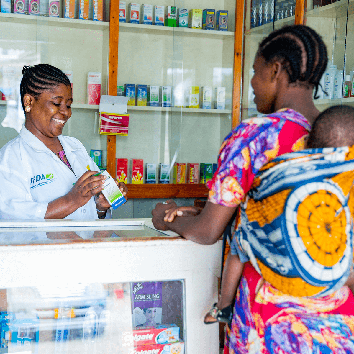 Building Integrated Systems for Financing Essential Medicines and Other Health Products — From Silos to Systems (Pharmacist in Tanzania dispenses medicine to a moth carrying her young child)