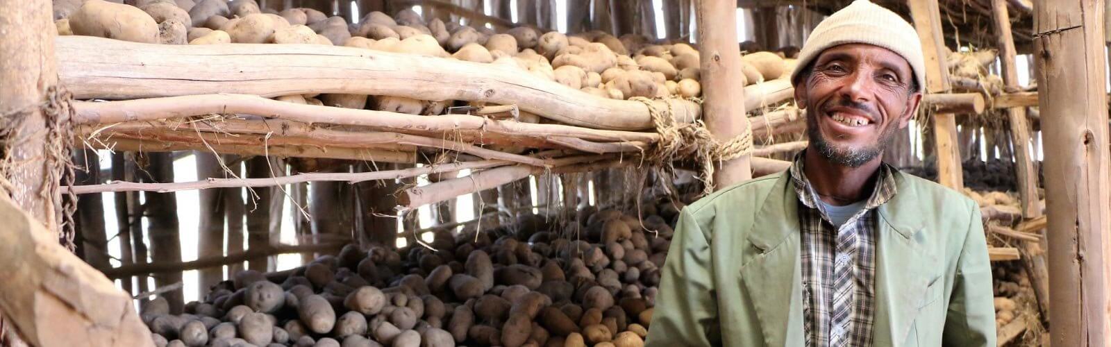a farmer posing in front of his harvest of potatoes