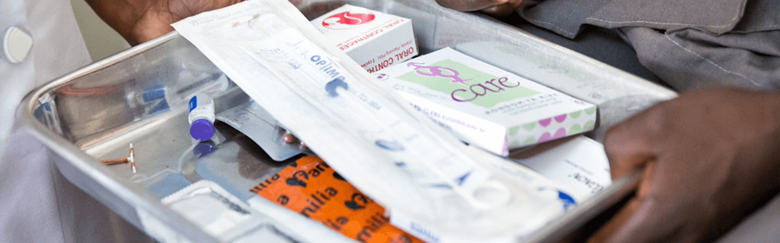 hands holding a tray of reproductive health commodities including IUDs, oral contraceptives and condoms